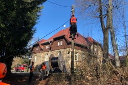 3 Bauarbeiter verlegen ein Kabel an einem Mast.